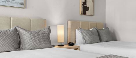 Et hotelværelse med to senge, et natbord med en lampe og et billede på væggen.