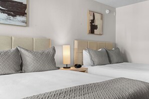Habitación de hotel con dos camas, una mesita de noche con lámpara y un cuadro en la pared.