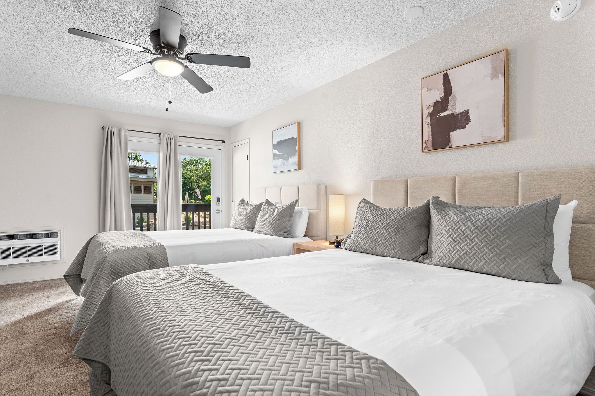 Une chambre d’hôtel avec deux lits, un ventilateur de plafond, une fenêtre avec des rideaux, une œuvre d’art accrochée au mur et une lampe de chevet.