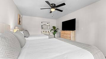 Quarto com uma cama, ventilador de teto, televisão e uma planta.