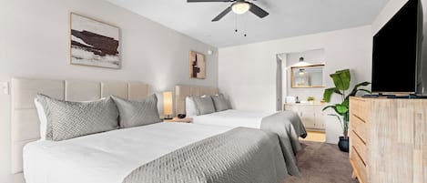 Ett hotellrum med två sängar, en takfläkt, en TV, en byrå och en växt.