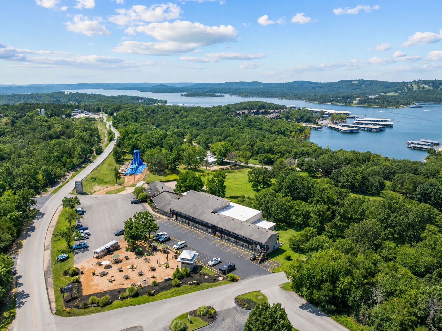 A large building with a parking lot, a water slide, and a view of a lake with boats.