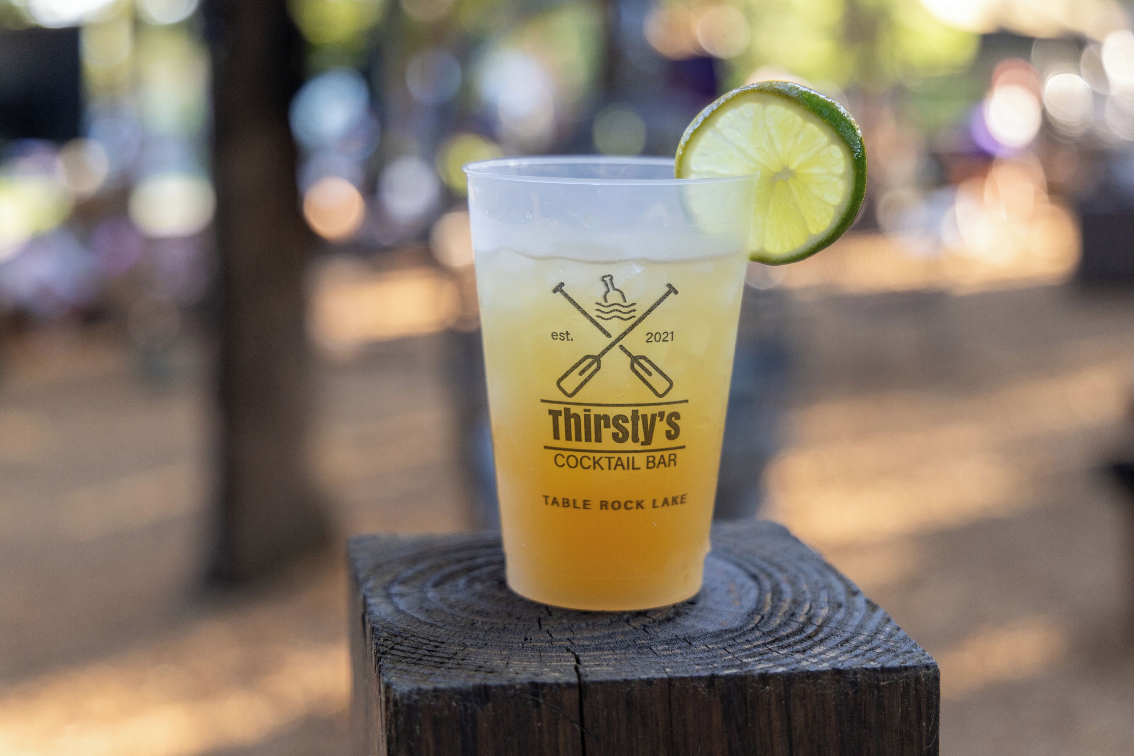 Un gobelet en plastique avec une tranche de citron vert, posé sur un poteau en bois. Le gobelet porte un texte et des illustrations indiquant qu’il provient du bar à cocktails Thirsty’s, fondé en 2021 et situé au bord du lac Table Rock.