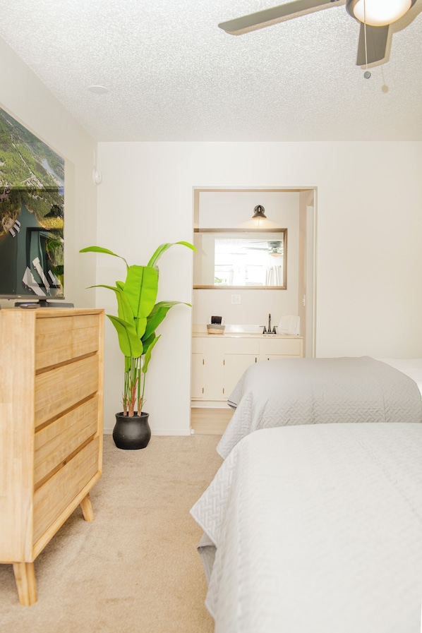 A bedroom with a bed, a dresser, a potted plant, a mirror, and a ceiling fan.
