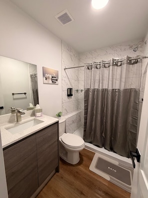 Ein modernes Badezimmer mit einer Marmordusche, einer Toilette, einem Waschbecken mit Spiegel und einer Duschvorhang.