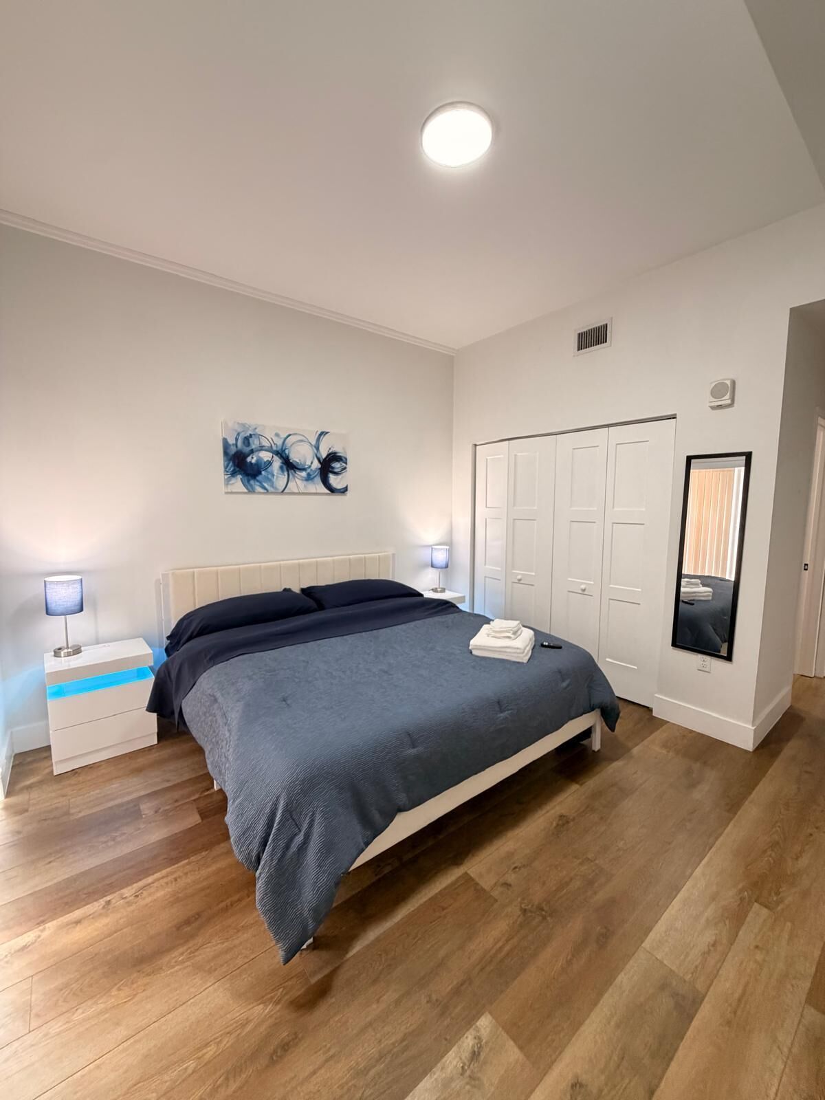 Une chambre à coucher avec un lit, des tables de chevet, une armoire, un tableau et un miroir.