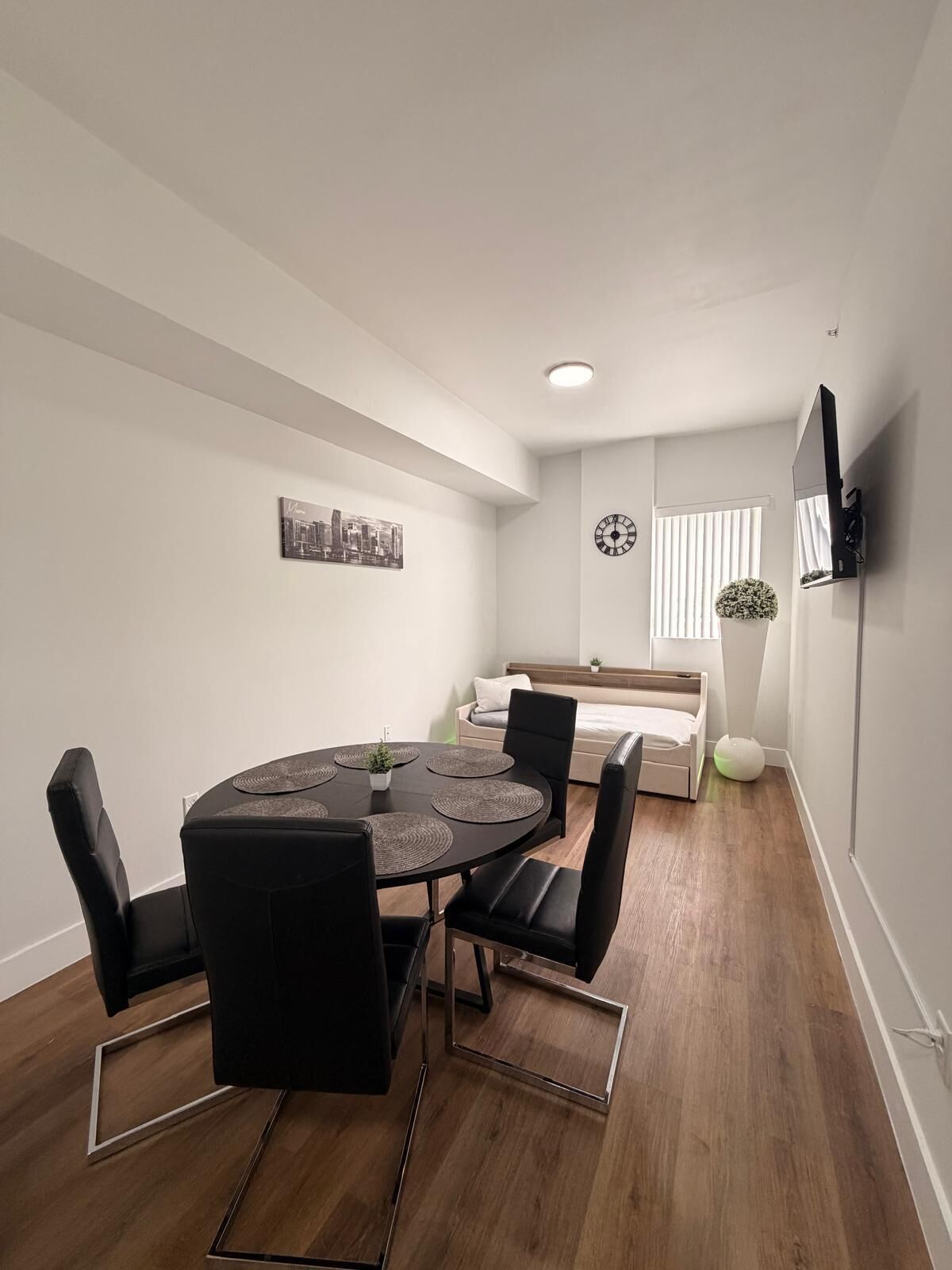 Une chambre moderne avec une table ronde, des chaises, un lit, un téléviseur et un tableau représentant un paysage urbain accroché au mur.