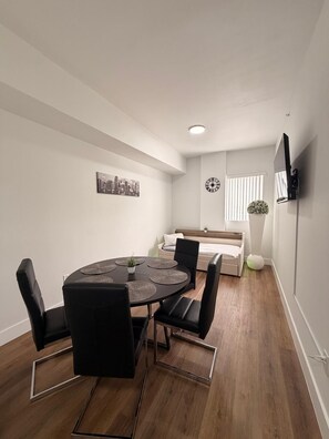 Ein modernes Zimmer mit rundem Tisch, Stühlen, einem Bett, einem Fernseher und einem Stadtbild an der Wand.