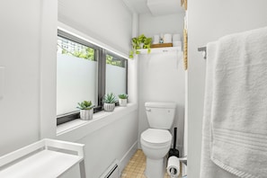 Ein modernes Badezimmer mit Toilette, Waschbecken, Fenster und Topfpflanzen.
