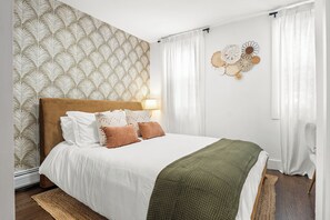 Ein Schlafzimmer mit strukturiertem Wandpapier, einem Bett mit weißer Bettwäsche und einer grünen Decke, sowie einem Wanddekor.
