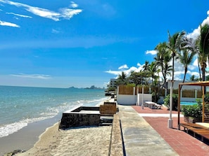 A beachside walkway with a pool area, palm trees, and a view of the ocean.