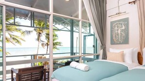 A room with a large window overlooking a beach, a bed with teal bedding, a wooden bench, and a wall-mounted artwork. - Wander at Bayside 19 | Upstairs Sea-View Room, bathtub & sunset (sleeps 4) (Hua Hin)