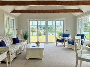 Ein Wohnzimmer mit einer Couch, Sesseln, einem Couchtisch und großen Fenstern mit Blick auf einen See und Gebäude.