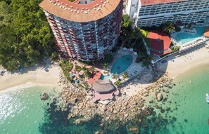 Ein Hochhaus-Hotel mit einem runden Pool, einem Strand und klarem, türkisblauem Wasser.