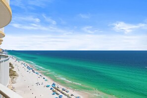 A beach view from a balcony with a clear sky, ocean, and beach umbrellas. - High-Floor Gulf View & Balcony - Emerald Skies (Panama City Beach)