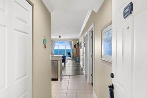 A hallway with a kitchen area, a dining table, and a view of the ocean. - High-Floor Gulf View & Balcony - Emerald Skies (Panama City Beach)