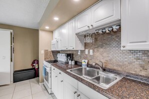 A modern kitchen with white cabinets, granite countertops, a double sink, and a brick backsplash.