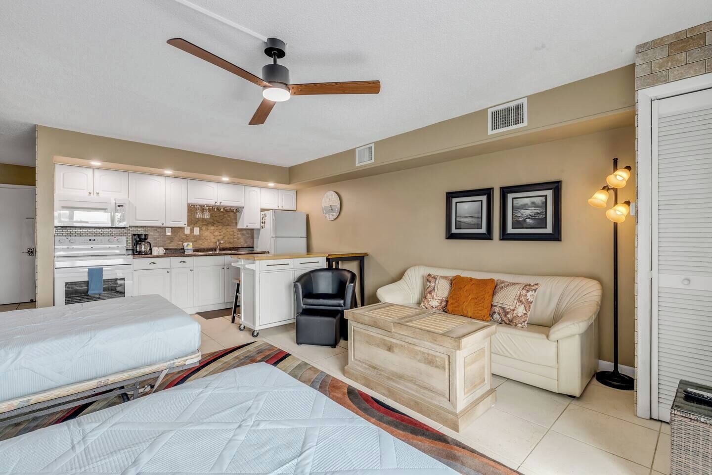 A compact room with a kitchenette, a sofa, a desk, and a ceiling fan.