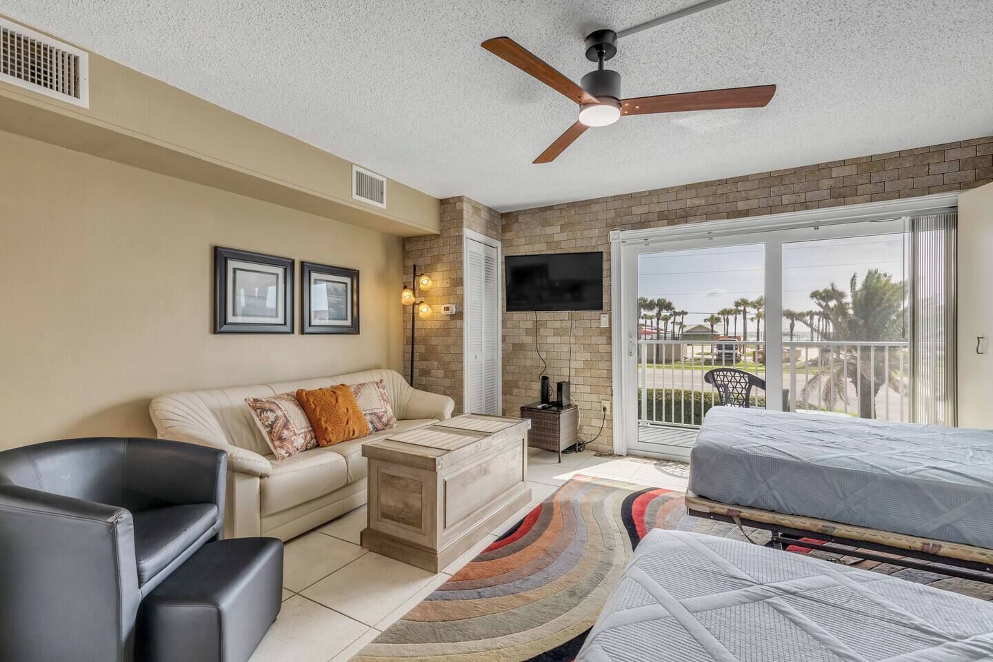 A room with a ceiling fan, a sofa, a bed, a TV, and a balcony with a view.