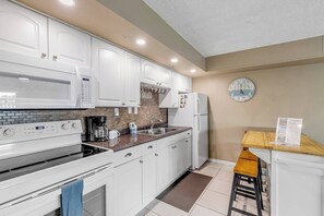A modern kitchen with white cabinets, a microwave, a stove, a coffee maker, and a refrigerator. - Mariners Cove Condo | Steps to Beach | Pool (New Smyrna Beach)