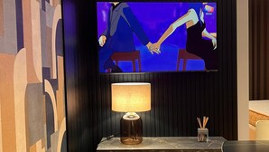 Moderni huone, jossa on tummalle seinälle asennettu televisio, lamppuvarustettu pöytä ja kuviollinen seinä.