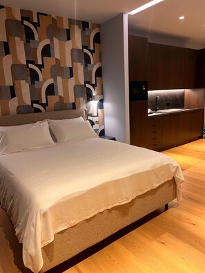 A modern bedroom with a large bed, a nightstand, and a built-in kitchen area.