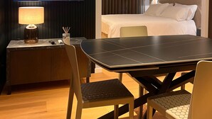 Hotellihuone, jossa on sänky, televisio, työpöytä lampun kanssa sekä ruokapöytä tuoleineen.