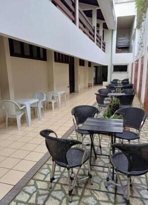 Um pátio externo com mesas, cadeiras, piso de azulejos e área coberta com guarda-corpo.