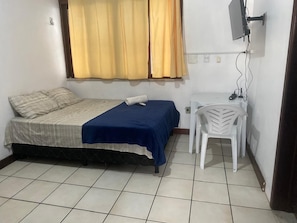 A bedroom with a bed, a chair, a TV, and a window with curtains. - Hotel Merlini  (Belém)