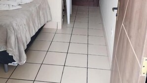 A narrow hallway with a bed on the left, a door at the end, and a white chair in the center. - Hotel Merlini  (Belém)