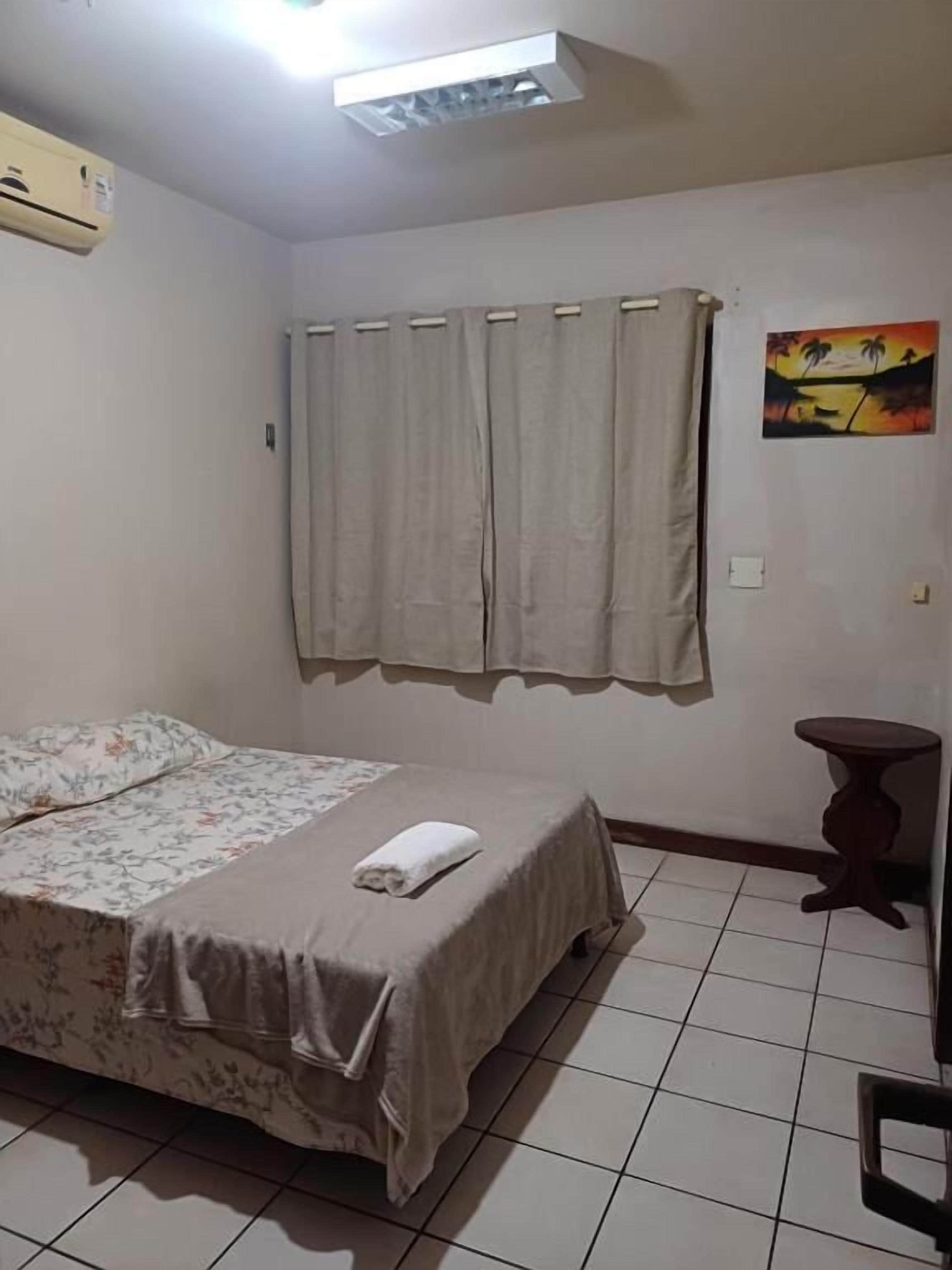 A bedroom with a bed, curtains, a small table, and a painting on the wall.
