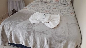 A neatly made bed with a floral-patterned bedspread, a folded white towel, and a small white table beside it.