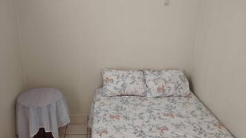 A small, single-bed room with a floral bedspread, a small round table with a white cloth, and a white shirt on the bed.
