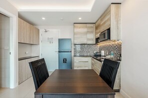 A modern kitchen with a dark wooden table, light wood cabinets, a blue door, and a tiled backsplash. - Luxury Babylon Sky Pool & Ocean View C189 (Tambon Rawai)