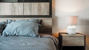 Una cama bien hecha con ropa de cama estampada, una lámpara de noche y un cabecero de madera.