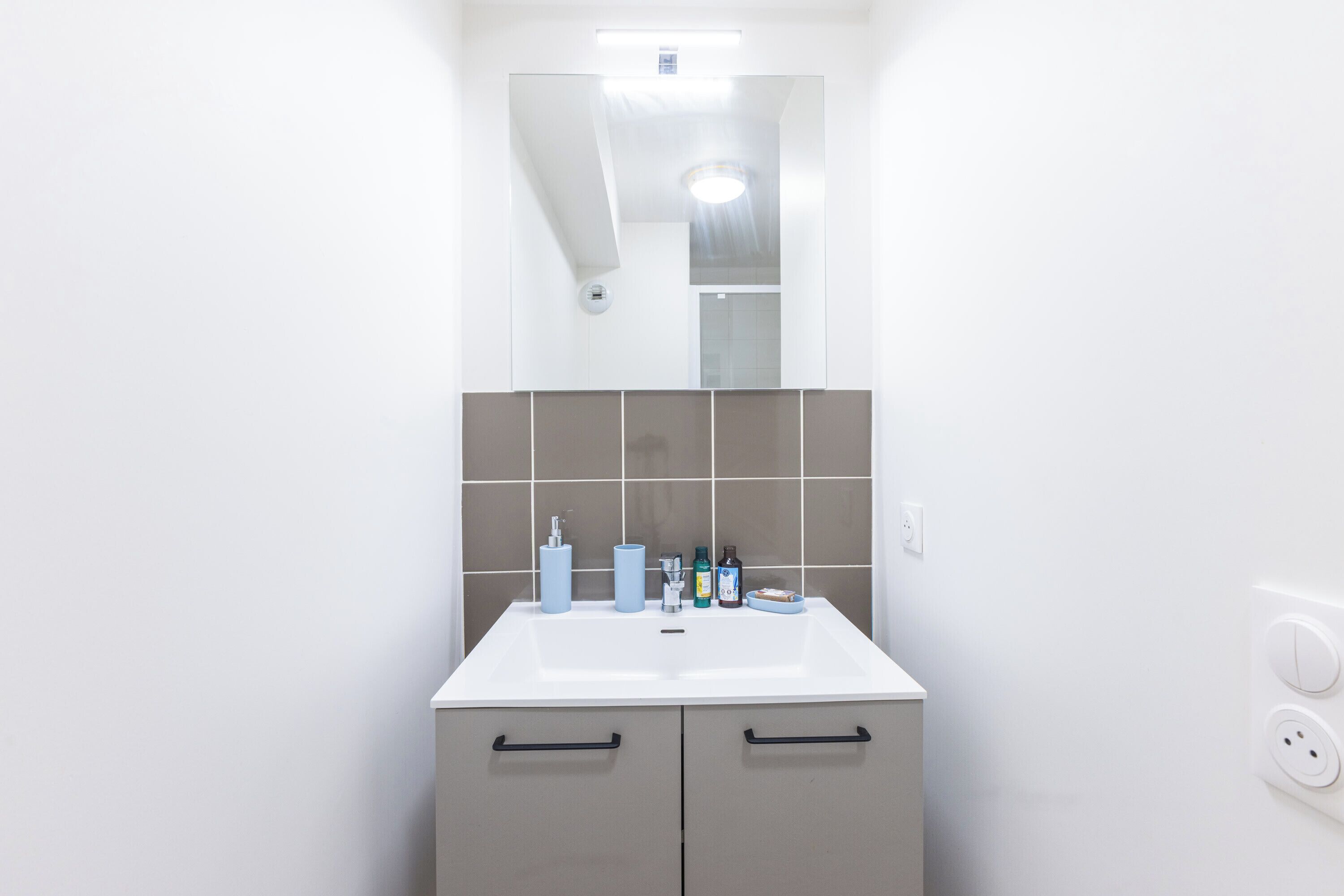 A bathroom with a white sink, two drawers, a mirror, and a tiled backsplash.