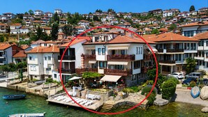Un hotel costero con varios balcones, un muelle con sillones de descanso y una vista despejada del barrio residencial circundante.