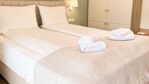 Una cama bien hecha con sábanas blancas, una lámpara de noche y una toalla doblada sobre la cama.