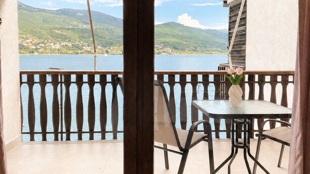Un balcón con vistas a un lago y montañas, una mesa con sillas y una cama con una toalla.
