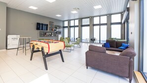 A spacious room with a foosball table, green chairs, a sofa, and large windows. - 310 - L'Obsidienne - (Achères)