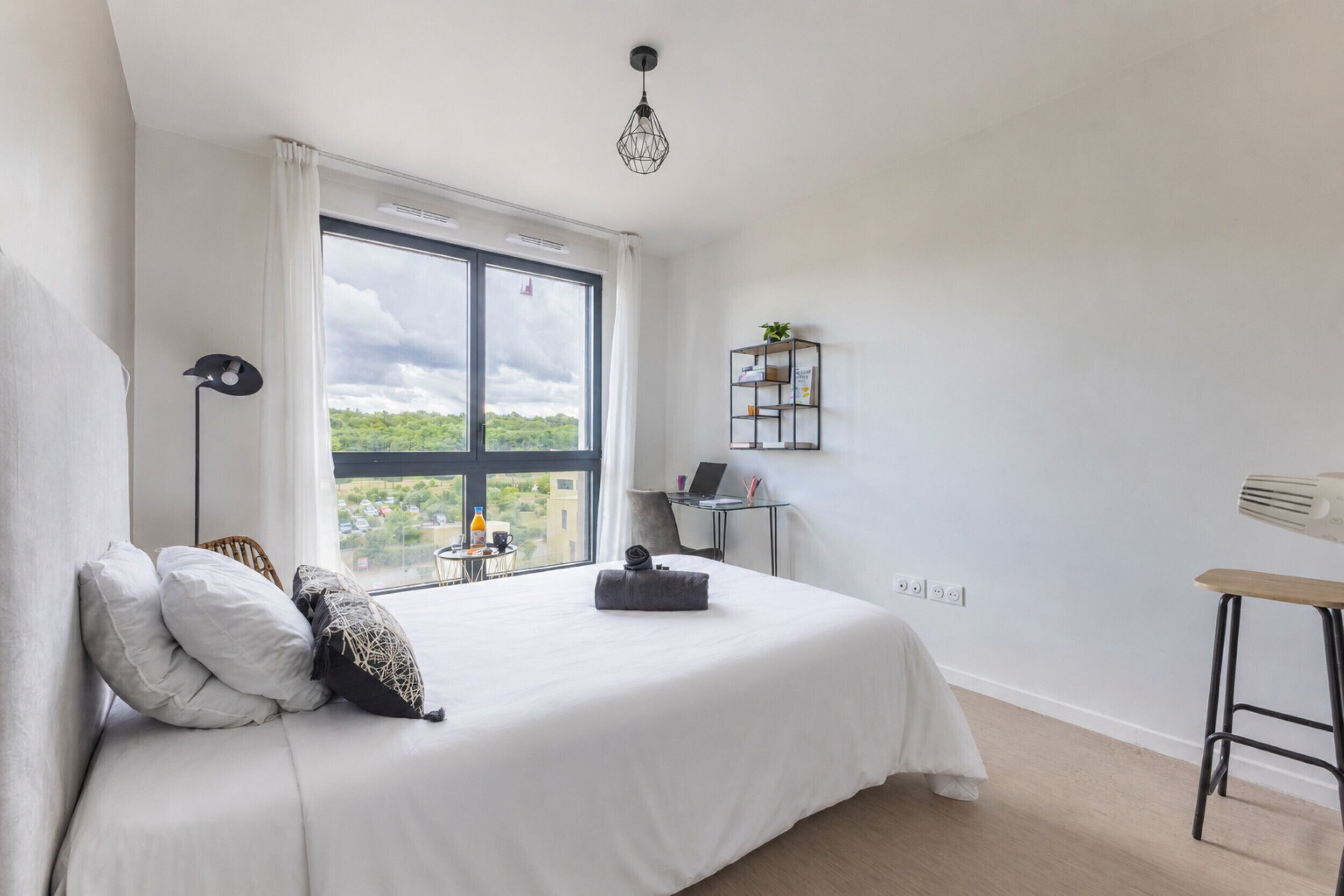 A bedroom with a large window, a bed, a desk, and a chair.