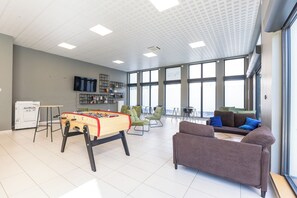 Ein geräumiges Zimmer mit Kicker, grünen Stühlen, einer Couch und großen Fenstern.