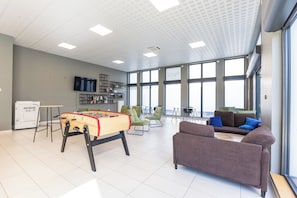 A spacious room with a foosball table, green chairs, a sofa, and large windows. - 408 - L'Obsidienne - Wifi (Achères)