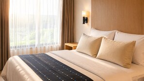 A hotel room with a bed, a nightstand, a wall-mounted lamp, and a window with curtains. - Adilia Hotel (Labuan Bajo)