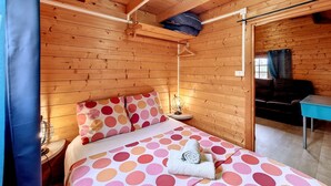 Una habitación de cabaña de madera con cama, lámpara colgante y ventana con cortinas.