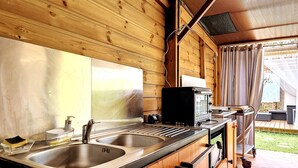 Una cabaña de madera con cocina, que incluye un lavamanos doble, estufa y microondas.