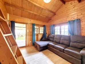 A wooden interior with a sofa, curtains, and a window. - Joli Cœur - Jacuzzi - Terrasse - Jardin (Saint-Louis)