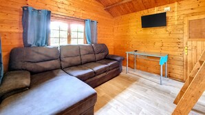 Interior de una cabaña de madera con un sofá seccional, una mesita y un televisor montado en la pared.