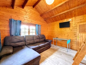 A wooden cabin interior with a sectional sofa, a small table, and a TV mounted on the wall. - Joli Cœur - Jacuzzi - Terrasse - Jardin (Saint-Louis)