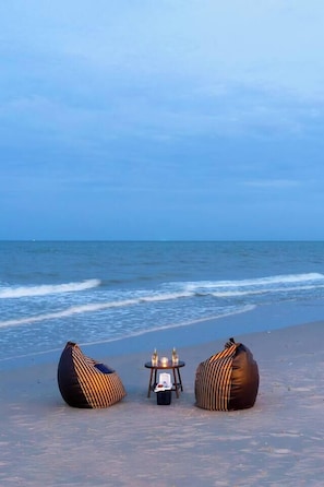 A beach with two bean bags and a small table with bottles.